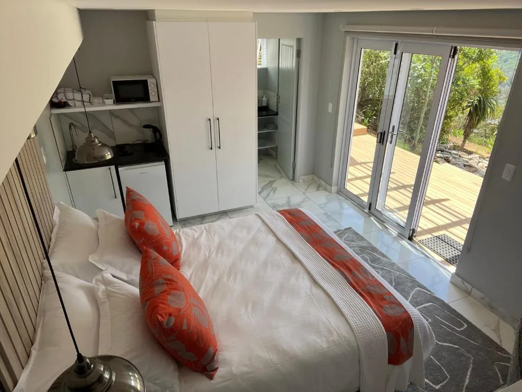 Modern bedroom with white bed, red pillows, and glass doors opening to deck