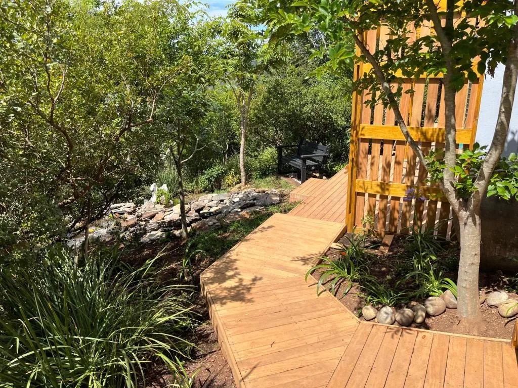 Wooden boardwalk pathway through lush garden with yellow pergola structure