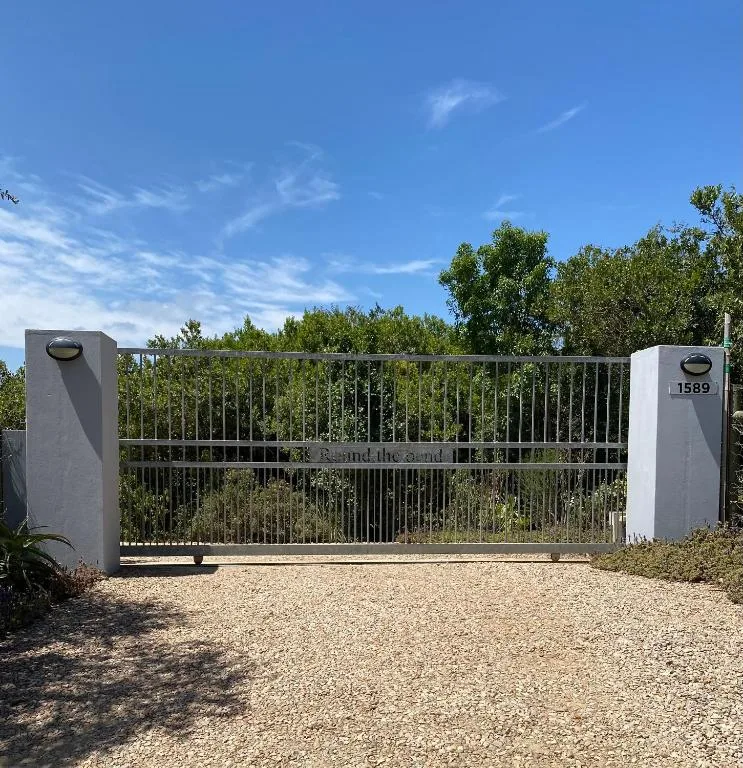 Modern metal driveway gate with white pillars and surrounding gardens