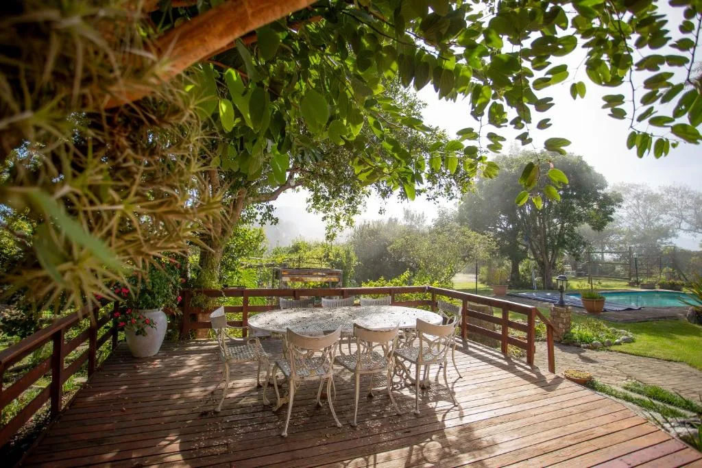 Wooden deck with dining table, chairs, lush greenery, and pool view