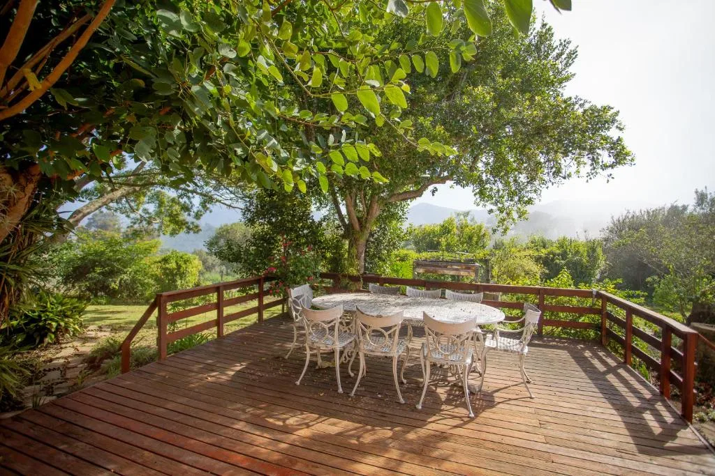 Wooden deck with dining table shaded by mature trees overlooking valley