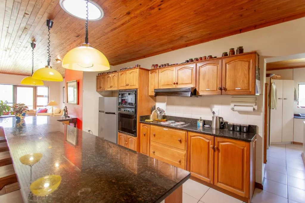 Spacious kitchen with wooden cabinetry, dark countertops, and yellow pendant lights