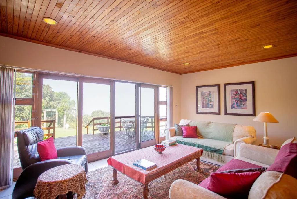 Bright lounge with wooden ceiling, sofas, and deck access overlooking gardens