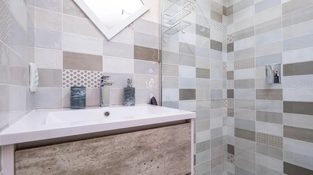 Modern bathroom with striped tile walls, white sink vanity, and glass shower enclosure
