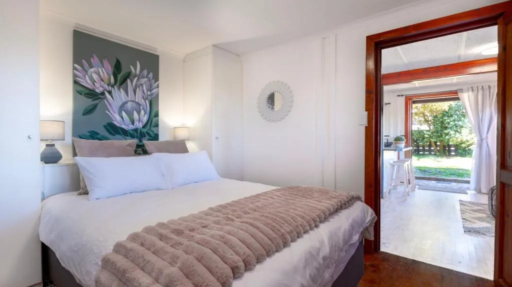 Bright bedroom with queen bed, floral artwork, and wooden door to garden