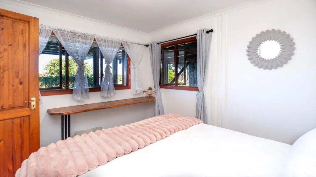 Bright bedroom with pink quilted bed and wooden window seat overlooking garden