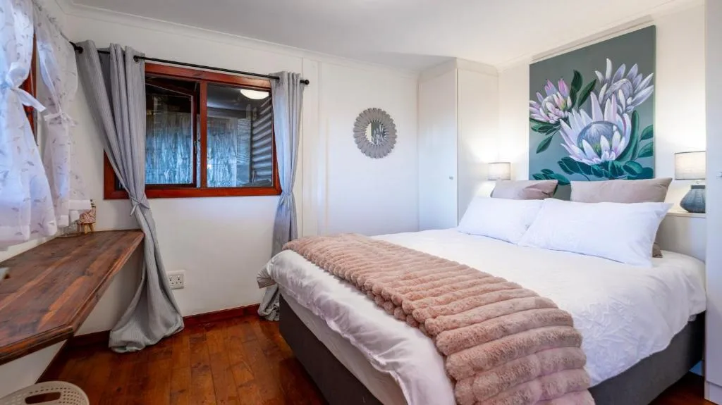 Bright bedroom with queen bed, floral artwork, and red-framed window overlooking garden