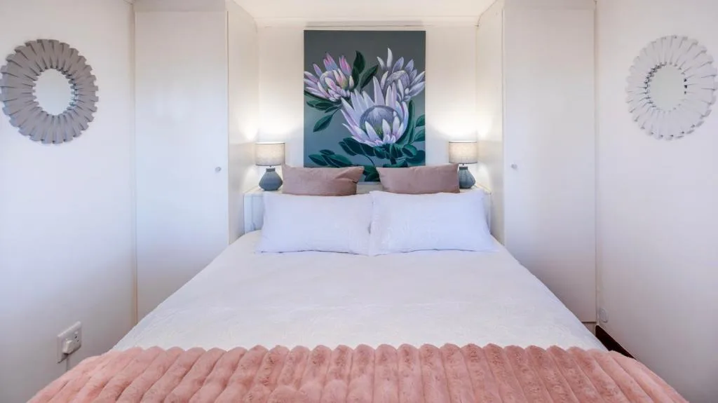 Bright bedroom with queen bed, floral artwork, and decorative wall mirrors