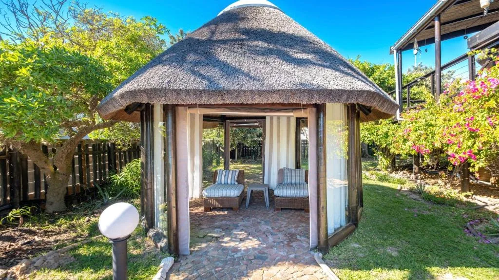 Thatched-roof gazebo with comfortable seating and garden surroundings