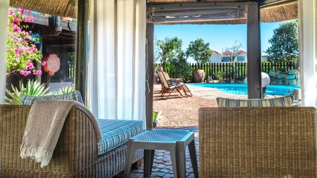 Covered patio with wicker seating overlooks pool and manicured garden