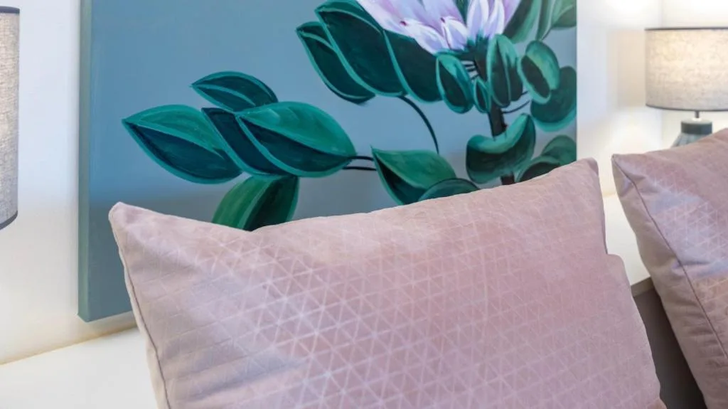 Decorative floral artwork and soft mauve pillows on bedroom furniture