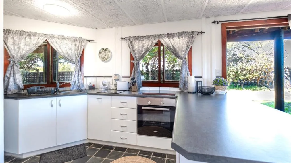 Modern kitchen with white cabinetry, black countertops, and large windows overlooking gardens