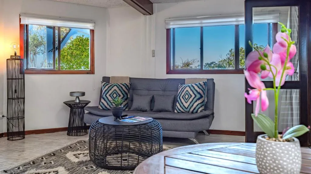 Modern lounge with grey sofa, geometric cushions, and large windows overlooking gardens