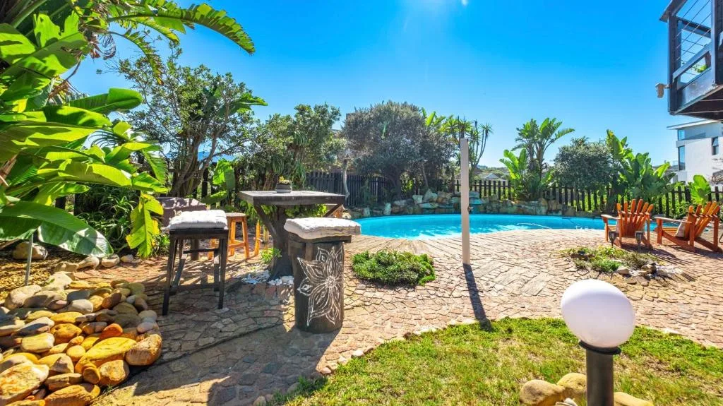 Sparkling blue swimming pool with tropical gardens and wooden deck seating area