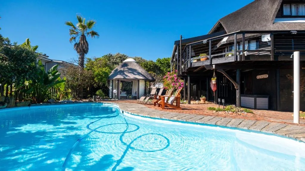 Crystal clear swimming pool with adjacent deck and thatched-roof house