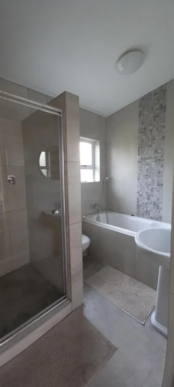 Modern bathroom with shower enclosure, bathtub, and mosaic tile feature wall