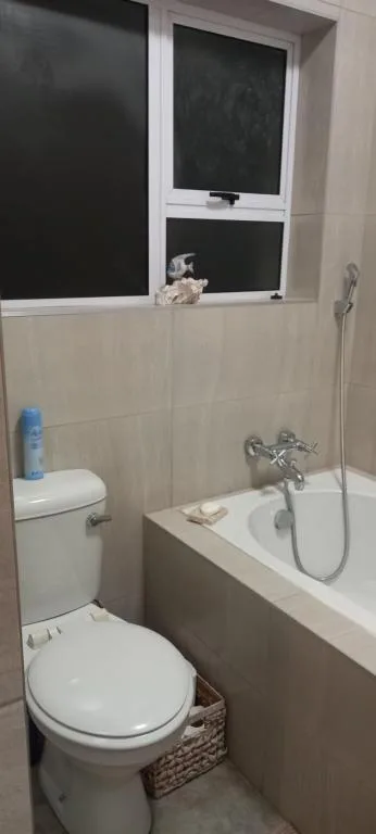 Compact bathroom with toilet, bathtub, shower fixtures, and window