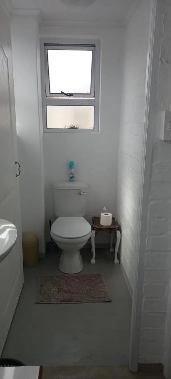 Compact bathroom with toilet, small window, and neutral tile flooring