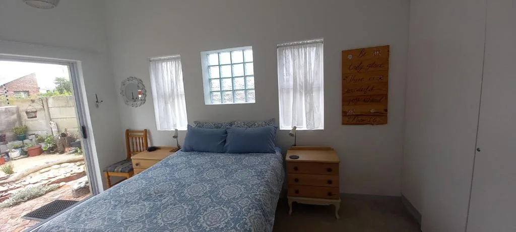 Bright bedroom with blue patterned bed, wooden nightstands, and garden view