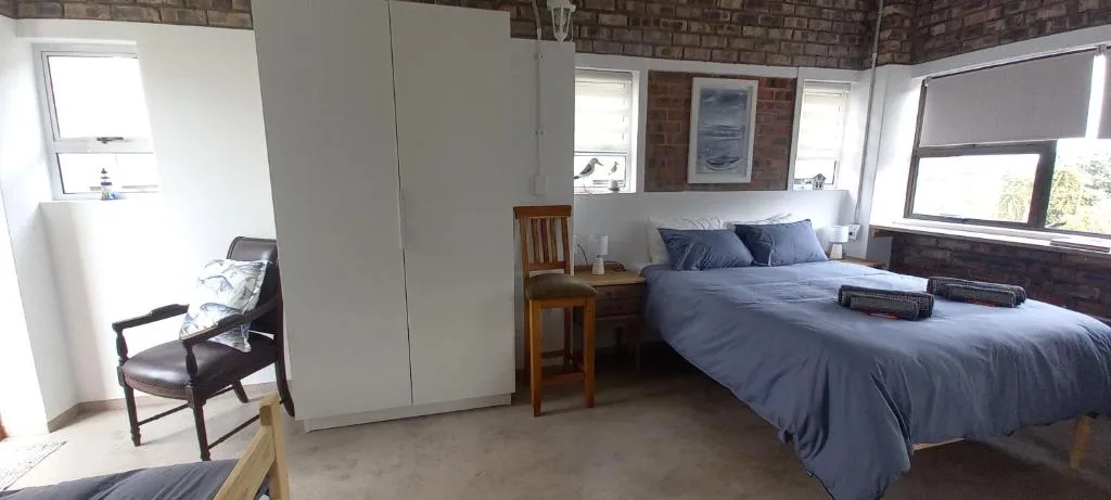Spacious bedroom with queen bed, blue linens, wooden furniture, and brick walls