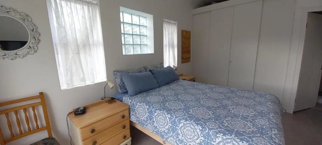 Bright bedroom with queen bed, wooden nightstand, and large windows