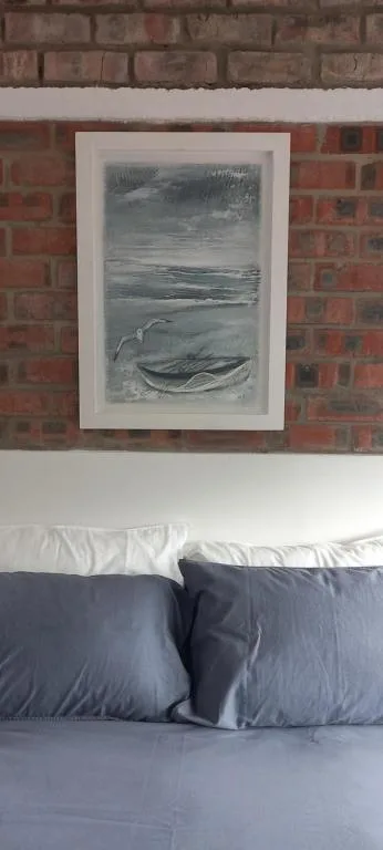 Bedroom with blue pillows and framed coastal artwork on brick wall