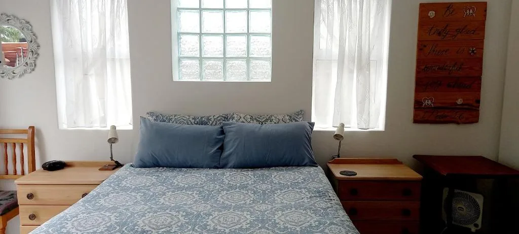 Bright bedroom with queen bed, blue pillows, wooden nightstands, and windows
