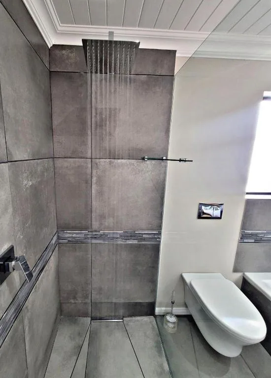 Modern bathroom with rainfall shower, gray tile walls, and white toilet