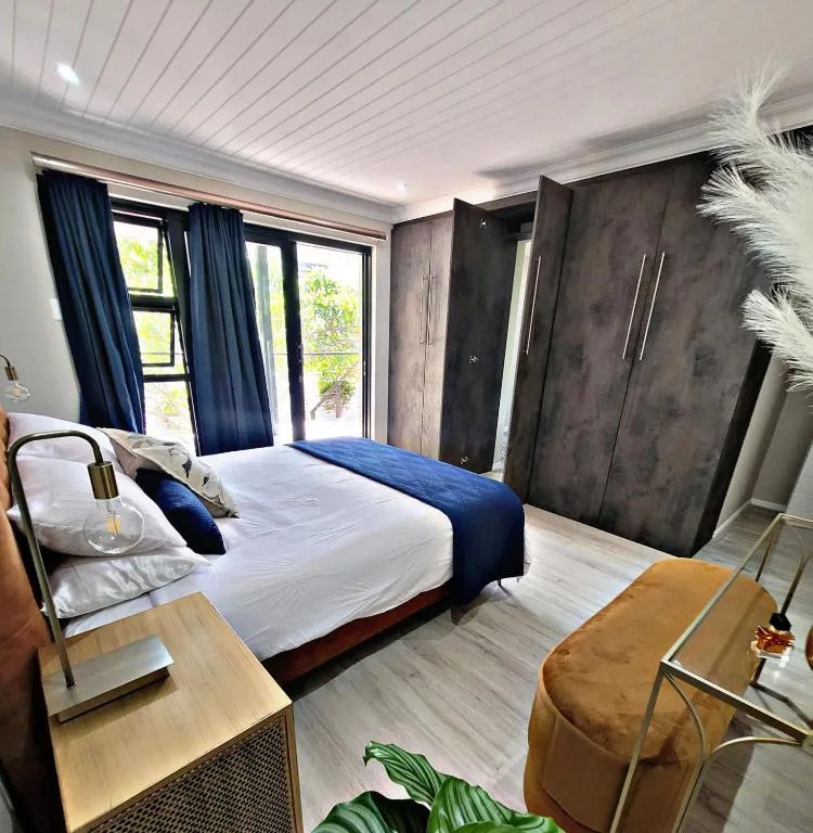 Modern bedroom with queen bed, blue accents, and garden views through doors