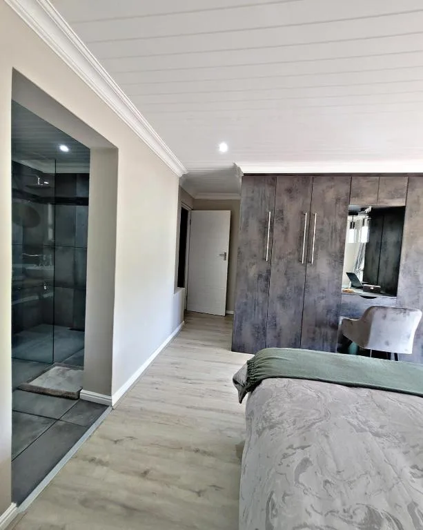 Modern bedroom with ensuite bathroom, bed with green throw, and built-in wardrobe