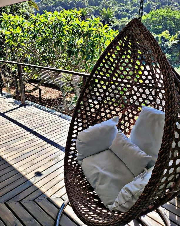 Hanging egg chair with white cushions on wooden deck overlooking green forest