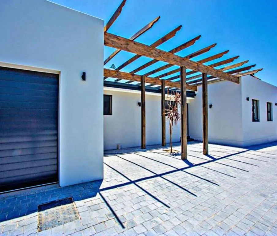 Modern patio with wooden pergola and paving, white building walls