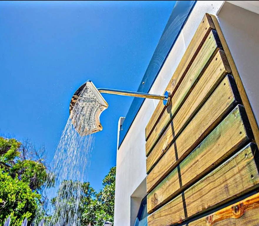 Outdoor shower with wooden slats and rainfall showerhead against blue sky