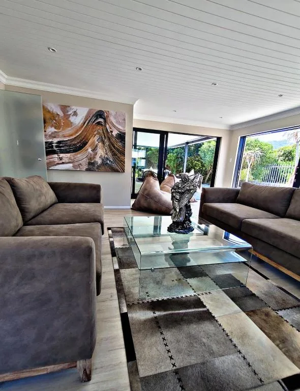 Modern lounge with grey sofas, glass table, and garden views through large windows