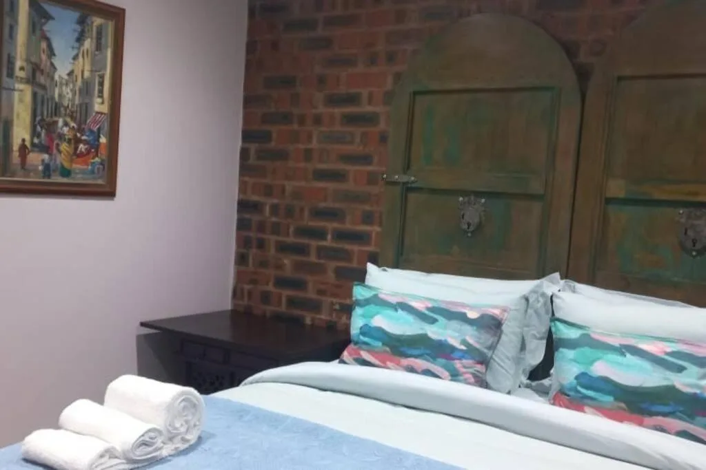 Bedroom with double bed, colorful pillows, towels, and exposed brick wall