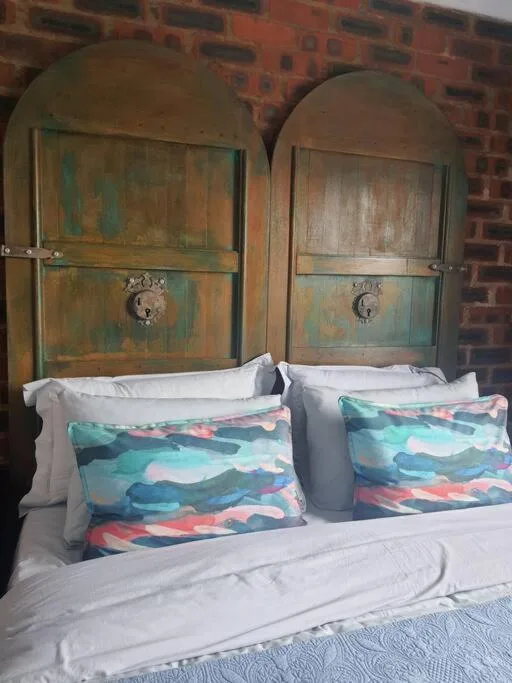 Bed with colorful patterned pillows and wooden arched headboards against brick wall