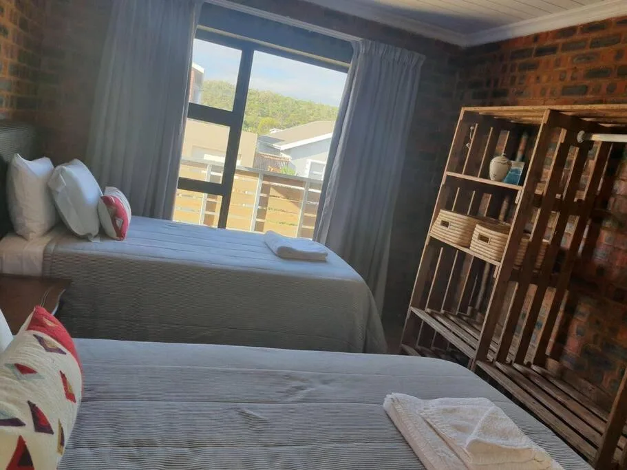 Bright bedroom with two beds and wooden shelving unit, garden views through windows