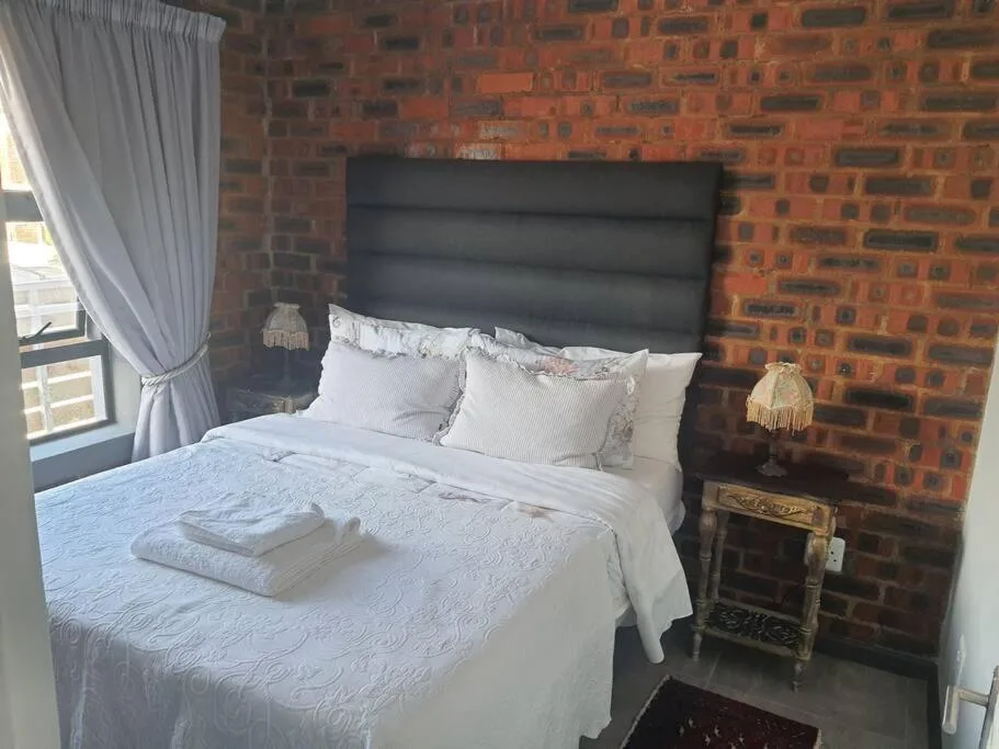 Bedroom with black headboard, white bedding, exposed brick wall, and window