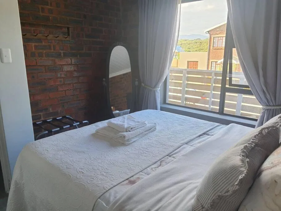 Bright bedroom with white bedding, red brick fireplace, and deck access