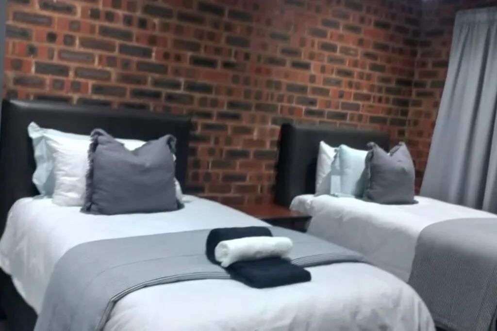 Twin beds with black headboards, white linens, and gray pillows against exposed brick