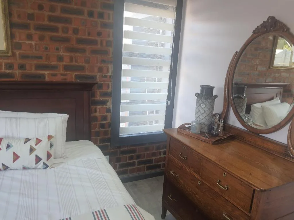 Bedroom with bed, wooden dresser, ornate mirror, and exposed brick wall