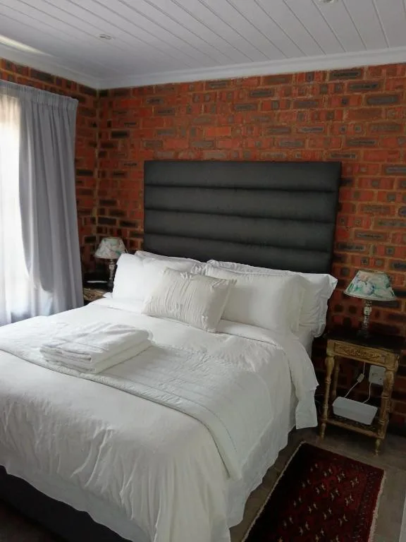 Bedroom with white bedding, black headboard, and exposed brick walls