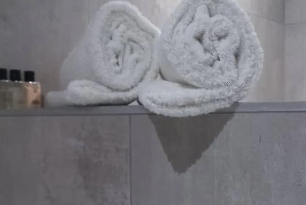 Rolled white towels displayed on bathroom shelf with toiletries