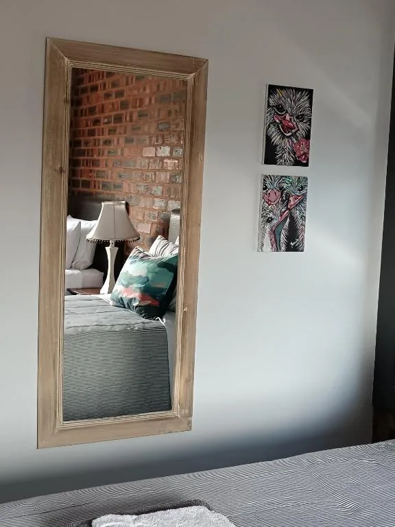 Large framed mirror reflecting bedroom with bed and exposed brick wall
