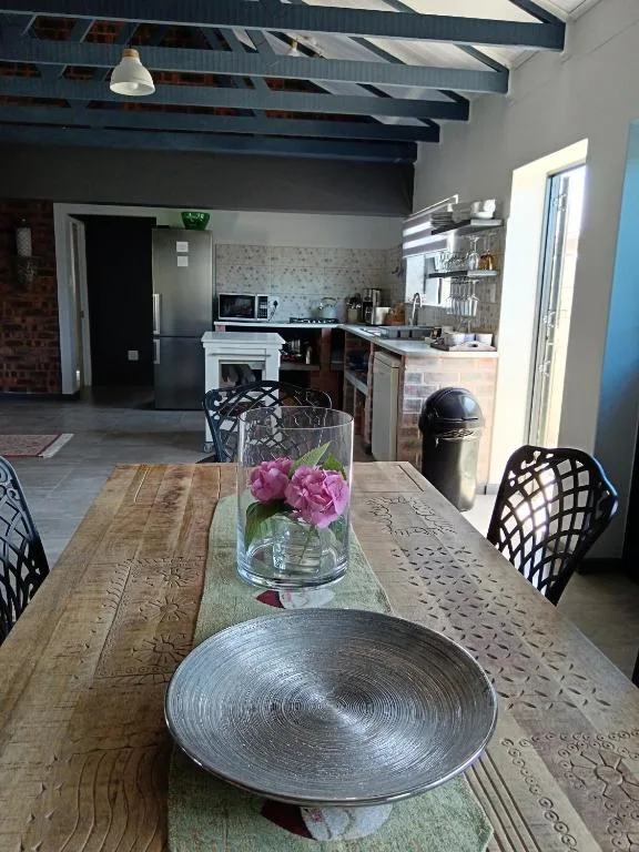 Wooden dining table with pink flowers and place settings, open-plan kitchen beyond
