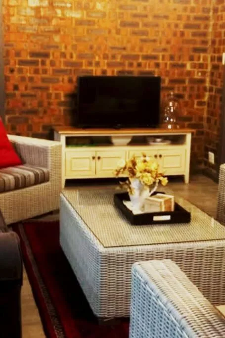 Bright lounge with TV on cream cabinet, wicker furniture, brick wall