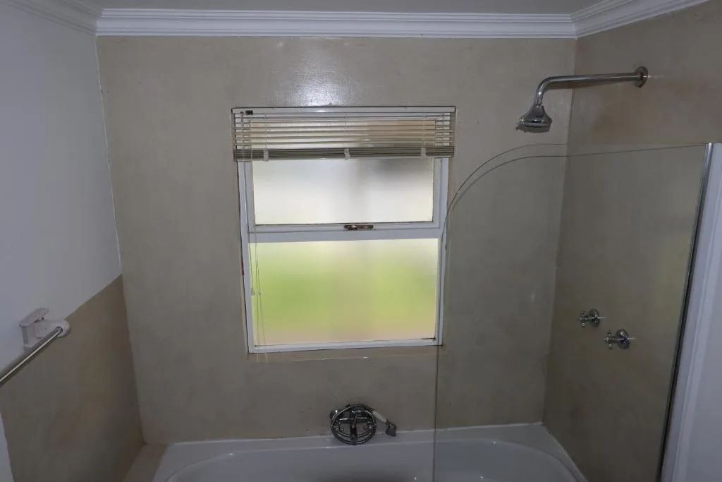 Modern shower enclosure with window, rainfall showerhead, and tiled walls