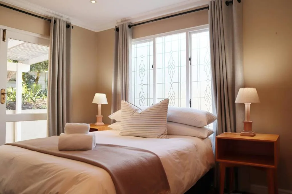 Warm bedroom with queen bed, striped pillows, and patio doors overlooking garden