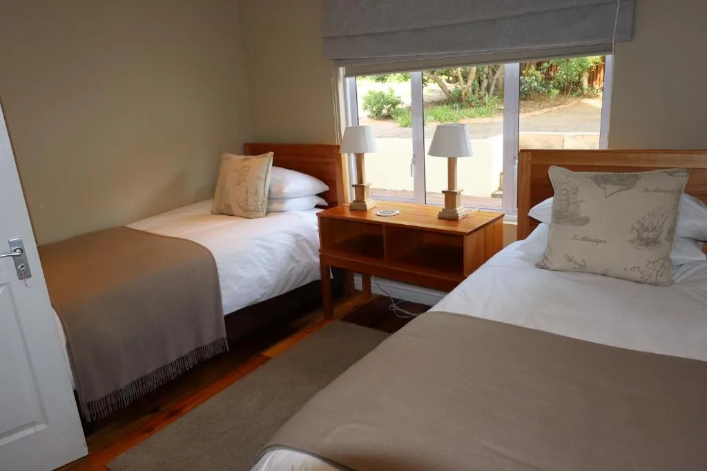 Twin bedroom with wooden beds, bedside table, and garden views through glass doors