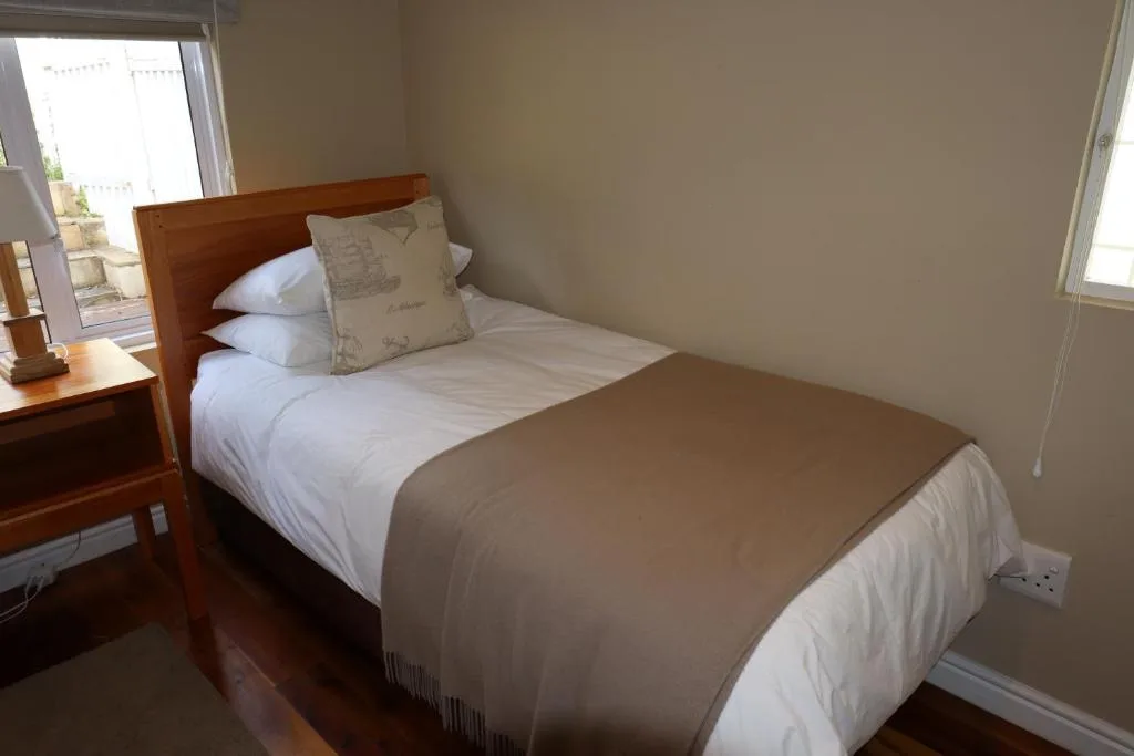 Bright bedroom with wooden bed frame and white linens, natural light from windows